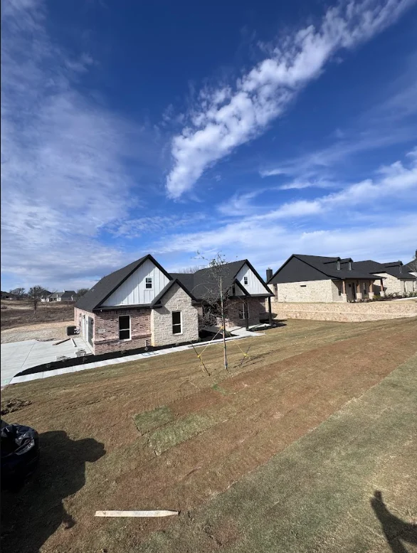 Newly graded residential lot with white and stone homes under construction in Weatherford subdivision