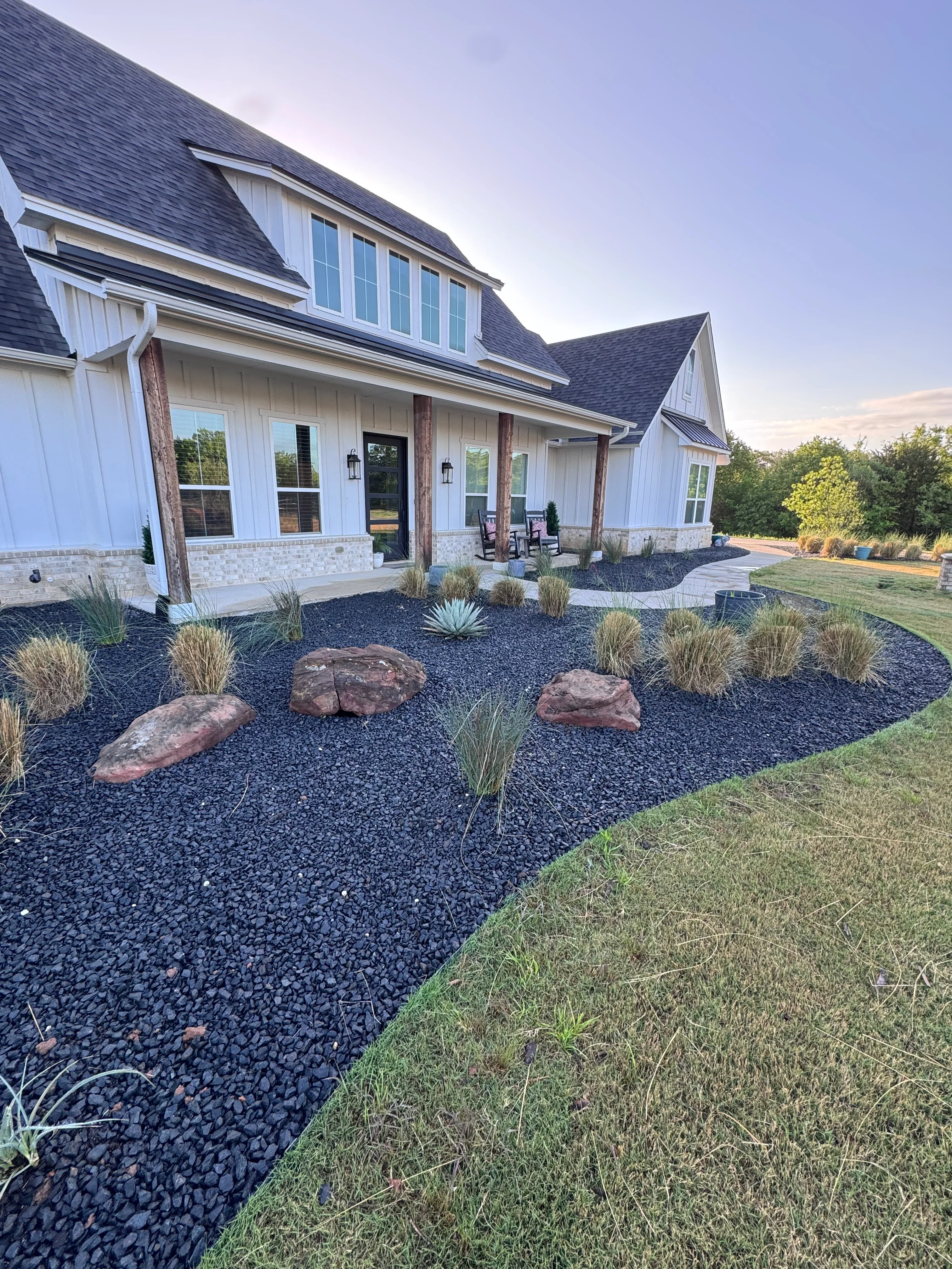 Modern home with dark rock hardscape, boulders, and ornamental grasses in front yard in Weatherford, TX