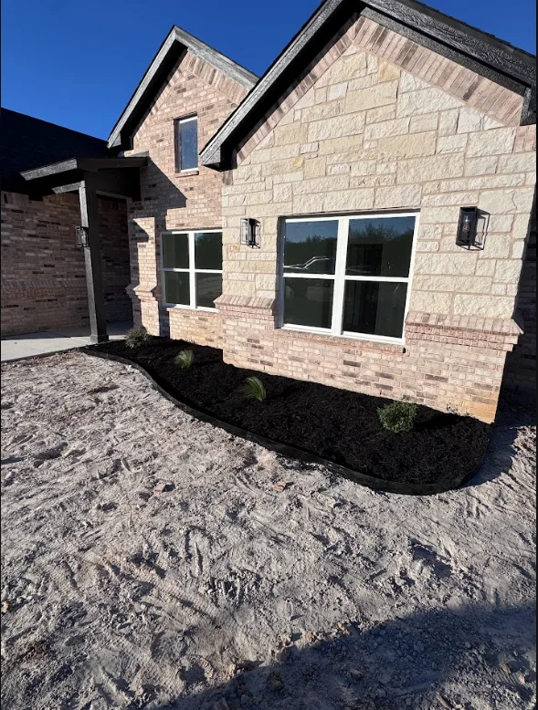 New brick home with freshly installed sod, black mulch beds, and foundation plantings
